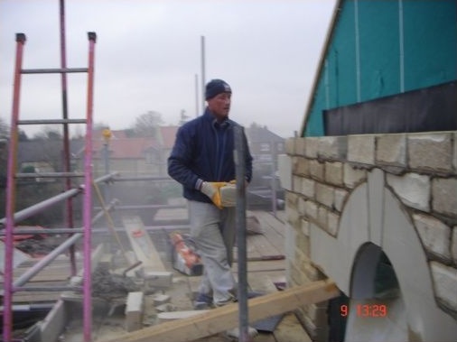 Stone mason ready to slot in the cut down stone above the featured stone arch